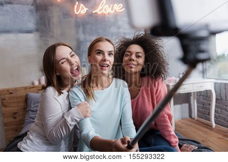 We taking selfie. Cheerful delighted young girls smiling and hugging each other while taking selfie and acting the ape at home