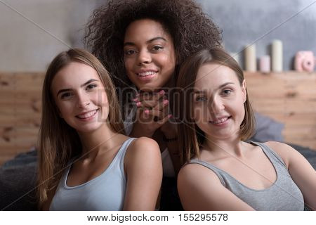 In a good mood. Pretty delighted young girls smiling and sitting