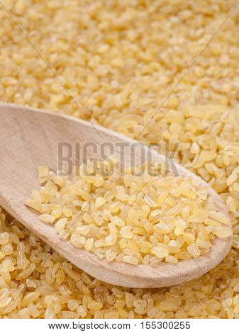 bulgur in wooden spoon close up. Vertical with copy space