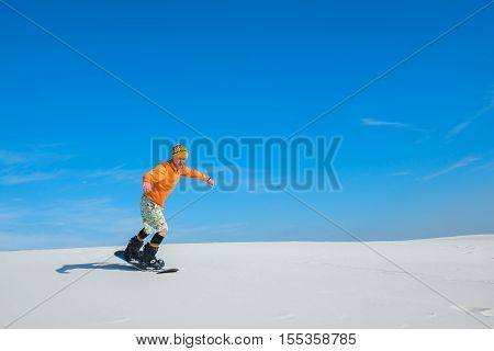 Sand boarder slides down the of the sand dune. Sand boarding in desert in the sunny day. Preparation for winter season snowboarding.