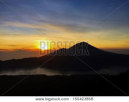 Sunrise in the mountains. Rising sun in orange and silver sky fluffy clouds distant mountains and volcanic lake.