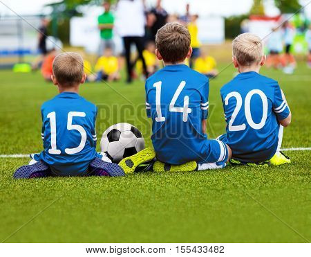 Children In Blue Sportswear Sitting On Soccer Pitch And Watching Football Soccer Match. Kids Soccer Tournament. Youth Soccer Background
