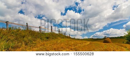panorama with fence and haycock on yellow field