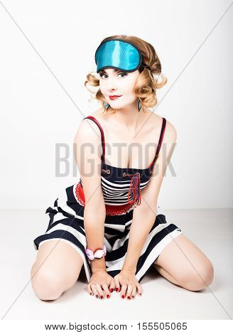 beautiful young woman in a striped dress and points for sleep, sitting on a floor and posing. sleeping eye covering mask.