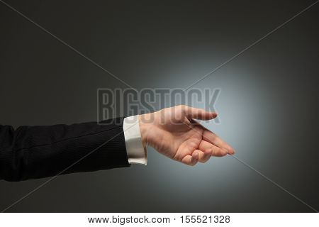 Dressed in a business suit caucasian male hand gesture of asking for the help or showing anything over the dark background