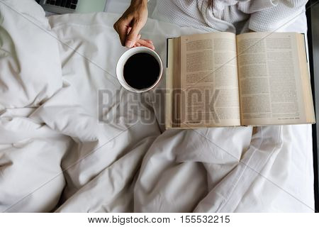 Beautiful asian female sitting on the bed with a cup of coffee and reading a book. Morning with a book and cup of coffee. Relaxing concept. Retro filter effectsoft focusselective focus.