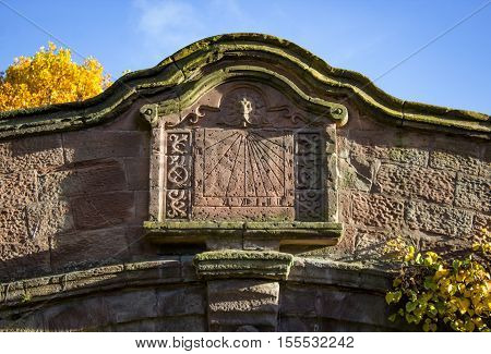A stone sundial carved into an old sandstone bridge in Port Sunlight, Wirral. A pretty picture with autumn colours on the leaves.