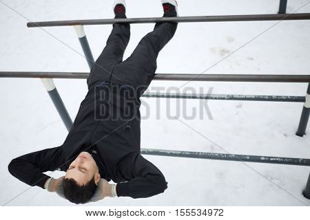 Man does exercises on parallel bars on sport playground in yard at winter