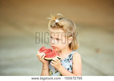 Adorable blonde girl eats a slice of watermelon outdoors