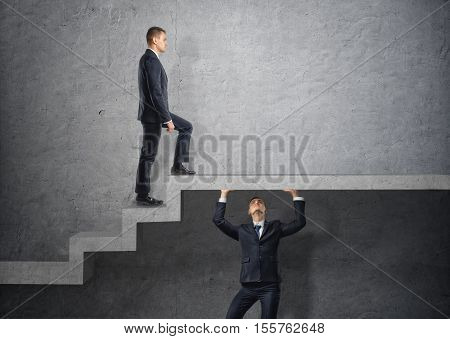 Businessman climbs the concrete stairs, which the other person keeps. Go over the heads. Do anything for the sake of personal gain. Social inequality. Boss.