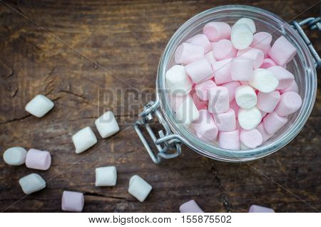 Pink and white mini marshmallows in a jar on an old rustic wooden table with space for text. Mini white and pink puffy marshmallows. Marshmallow concept. Copy space. Top view.