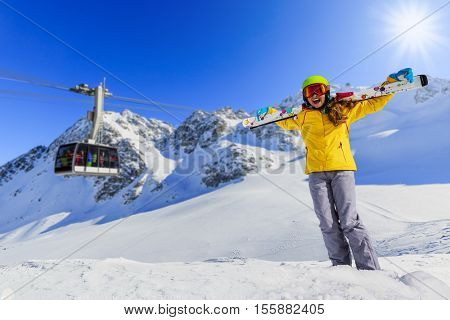 Smiling girl standing with ski and arms spreading wide open on the fresh powder snow at sunny day in mountains. Ski lift cable car in background. Switzerland, Verbier, Alps. 