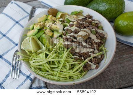 Green raw vegan zucchini pasta with lentils, pesto, tahini, avocado, olives and oil. Delicious food detox every day.