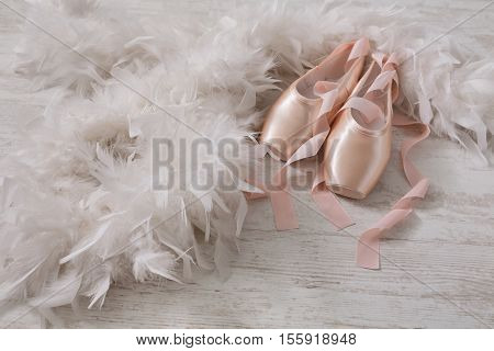 Pastel pink ballet shoes background. New pointe shoes with satin ribbon lay on white rustic shubby chic wood near feather boa, view with copy space