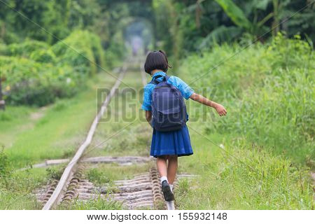 Thai schoolgirl in traditional costume walking and balancing on the railway of the Talat Phlu district in Bangkok.