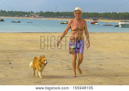 PORTO GALINHAS, BRAZIL, JANUARY - 2016 - Old man walking forward with his dog at tropical beach in Porto Galinhas Pernambuco Brazil