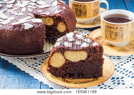 Baking in multicooker. Delicious homemade chocolate cake with curd-coconut balls on a blue wooden table. Decorated with coconut crunch. Served with tea. Selective focus