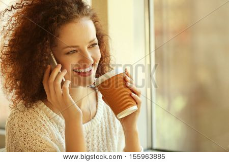 Attractive woman savouring coffee and speaking by cellphone in cafe