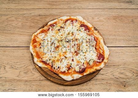 Delicious round pizza with salami and pickles served on a wooden plate on old wood table