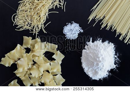 Three Different Types Of Pasta, Pile Of Flour, Salt And Pepper Are Laid Out On Black Background