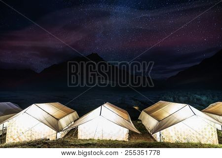 Camping Under Colourful Sky Full Of Stars. Glowing Tents With Silhouette Mountains And Sky Full Of S