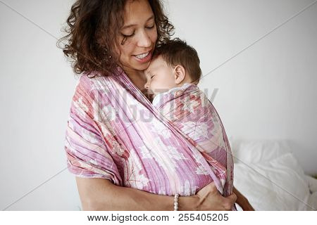 Indoor Shot Of Beautiful Young Mixed Race Mother Smiling, Watching Her Adorable Newborn Infant Son S