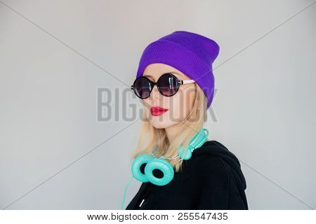 Young Girl In Purple Hat With Headphones And Sunglasses On Grey Background. Melomaniac Person