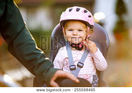 Portrait Of Little Toddler Girl With Security Helmet On The Head Sitting In Bike Seat And Her Father