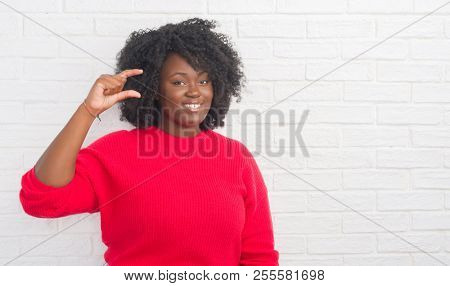 Young african american plus size woman over white brick wall smiling and confident gesturing with hand doing size sign with fingers while looking and the camera. Measure concept.