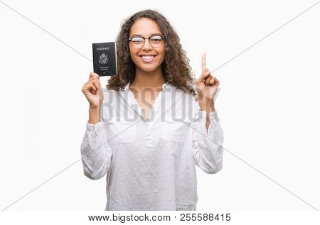 Young hispanic woman holding passport of United States of America surprised with an idea or question pointing finger with happy face, number one