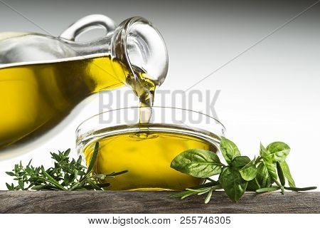 Bottle Of Virgin Olive Oil And Herbs Pouring In A Bowl Close Up