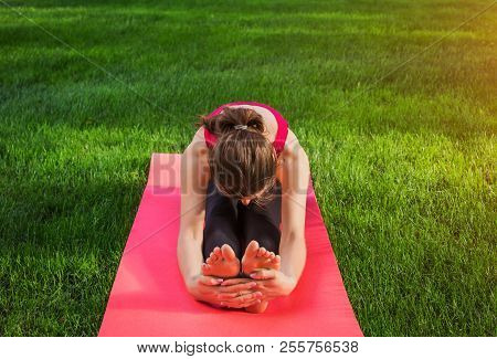 Seated Forward Bend Pose. Woman Practicing Yoga Sitting On Mat In The Park