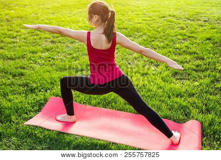 Warrior Pose. Woman Practicing Yoga Sitting On Mat In The Park. Sport And Health Concept