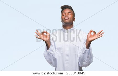 Young arabic african man wearing traditional djellaba over isolated background relax and smiling with eyes closed doing meditation gesture with fingers. Yoga concept.