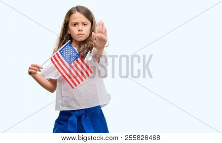 Brunette hispanic girl holding flag of United States of America with open hand doing stop sign with serious and confident expression, defense gesture