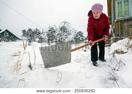 Elderly woman cleans snow near the his rural house at vinter.