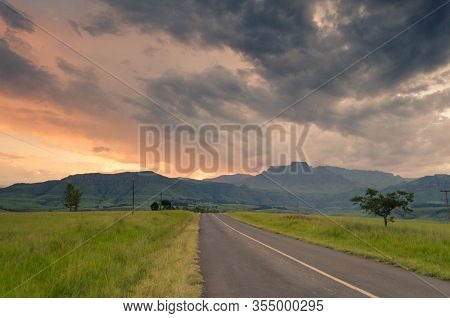 A Road Leading Towards Champagne Castle Mountains, At Sunset In Central Drakensberg, Near Winterton,