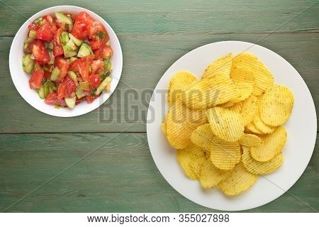 Potato Chips On A White Plate With Vegetarion Salad. Chips On A Green Wooden Background Top View.