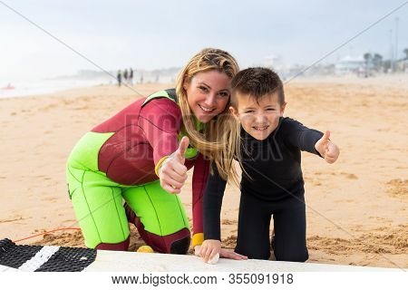 Mother And Son In Wetsuits Showing Thumbs Up. Happy Mother And Cute Little Son Waxing Surfboard And 