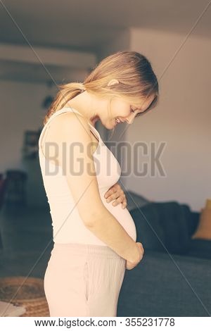 Happy Expectant Mother Talking To Her Baby Bump. Cheerful Pregnant Young Woman Looking At Her Belly 