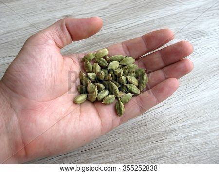 Close Up Of Green Cardamon Seeds On Male Hand With Wooden Background.