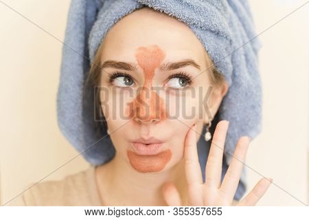 A Beautiful Girl With A Towel On Her Head Makes A Multi Mask On The T-zone Of Orange Color With A Sc
