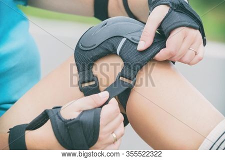 Woman rollerskater putting on knee protector pads on her leg
