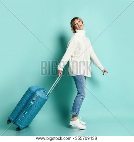 Attractive Blonde Girl In White Sweater, Jeans And Sneakers. She Is Smiling, Posing With Suitcase St