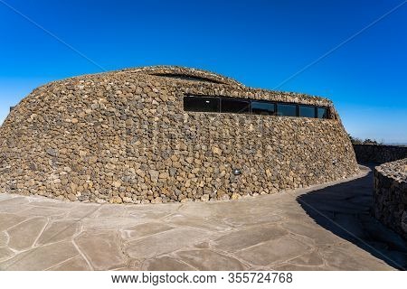 Modern Public Architecture. Curved Inclined Wall Made From Stone. The Rock Shed On Sunny Day.
