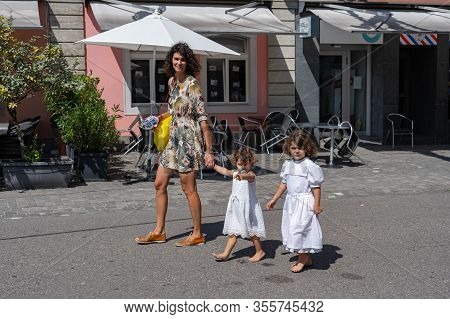 Young Mother With Two White Dressed Little Girls Walking At Sunny Day Through The Streets Of The Old