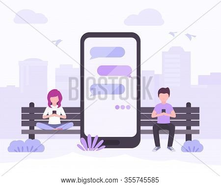Young Woman And Young Man Sitting In City Park Near Big Smartphone With The Message Bubbles On Scree