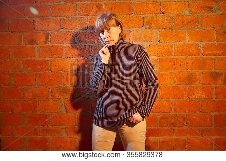 A Middle-aged Woman Poses Showing Clothes Near Red Brick Wall. An Inept Model In An Inept Shoot