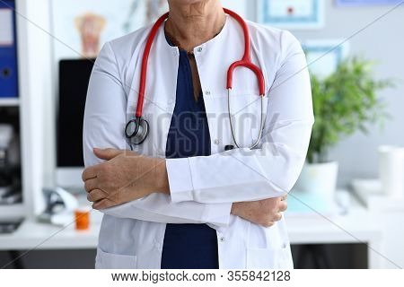 Close-up Of Elderly Woman Working In Hospital. Lady With Folded Hands. Experienced Doctor Using Spec