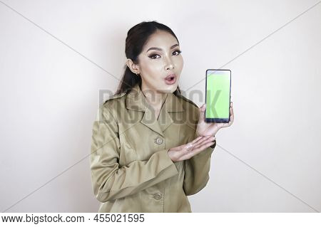 Shocked Asian Woman Wearing Brown Uniform Pointing Finger At Green Screen On Smartphone In Her Hand